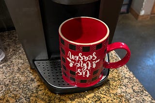 Christmas themed coffe mug, upside down on a Kuerig brewer, coffee spilled all over granite counertop.