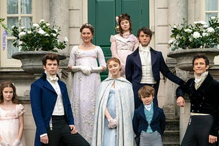 A family with 4 women and 4 men stand in front of a house with fresh flowers near them. They are dressed in clothing of the 1800s. Bridgerton, Netflix, historical, romance, drama, bodice ripper, Shonda Rhimes