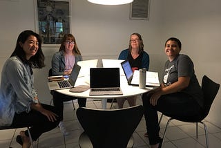 Four writers together at a circular table with their laptops open. They are the Foothill Poets, 2018