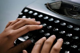 Hands touch the letter keys on a typewriter.