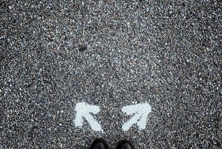 A man standing in front of two arrows point different directions.