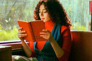 A woman reading a red book on a bus.