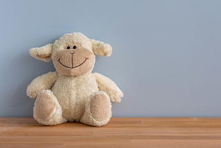 Picture of a smiling Teddy bear against a blue wall.