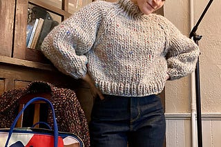 A woman with short hair wears a hand-knit gray sweater made from thick wool yarn