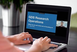 Hands on the keys of a silver laptop with a slide that says GDS Research Operations.