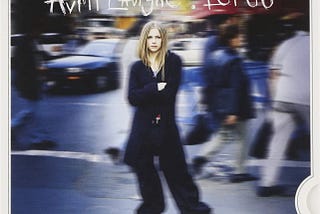 The album cover of Avril Lavigne’s “Let Go.” Lavigne stands in a crowded street with people and cars blurred behind her.