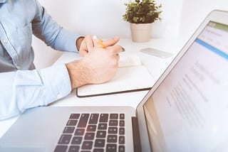 guy writing on a book right next to a computer