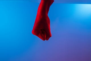 A fist bathed in red light in front of a blue background.