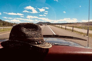 Straw hat resting on the dashboard of a car rolling on a road, sunny day blue skies.