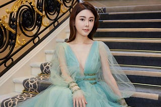 A picture of Abby Choi dressed in a gorgeous blue dress seating on stairs.