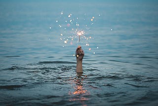 A hand in the sea holding up a sparkler