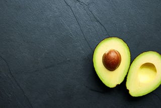 A photo of an avocado cut carefully in half, against a dark background.