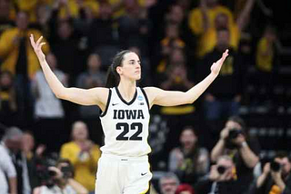 Basketball phenom Caitlin Clark poses with outstretched arms after facilitating an amazing play.