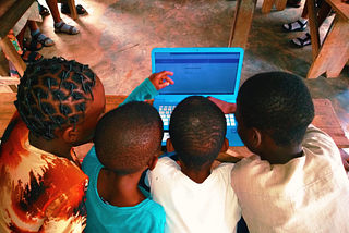 Four learners engaging with Kolibri through a laptop computer in an Nigerian classroom.
