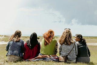 Group of women presenting women with long hair and scarves sitting on the edge of a beach