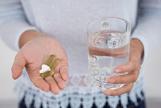 Woman holding a glass of water in her left hand and multiple pills in her right.