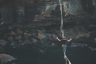 A man walking across a tightrope hanging over a chasm