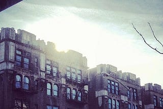 sun piercing through clouds above intricately designed building tops in Washington Heights near the home of Jose Toribio