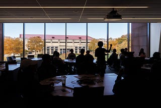 An instructor gestures during a class with students backlit with Allen Fieldhouse in the background