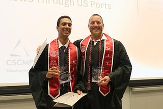 Yassine Lahlou-Kamal and Kevin Power in graduation regalia pose together holding clear glass awards