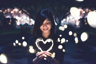 Woman holding a light garland heart at night time.
