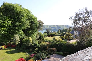 Photograph of trees and sweeping lawns with a view of the Helford river in the distance.