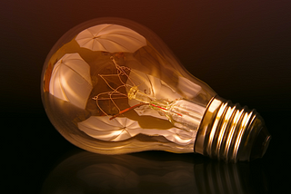 A lightbulb lying on its side, with white umbrellas reflected in the glass.