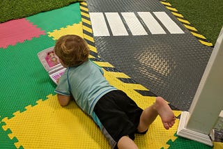 Young child laying on their stomach in the middle of a play area, typing away at a fake laptop.