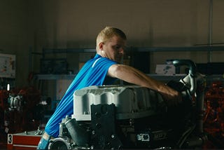 A side profile of an auto mechanic student working on an engine