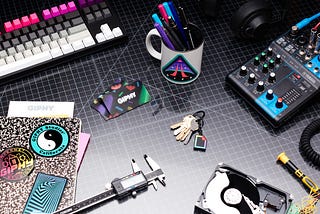A desk with a notebook, keys (including a GIPHY logo keychain), pens, and a colorful keyboard, all arranged on a black and white checkered desk with GIPHY branding in the background.