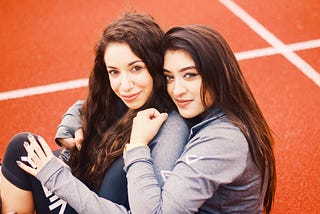 two girls with brown hair sitting on orange painted floor hugging