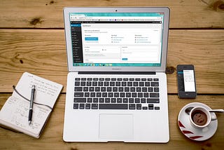 Laptop showing Wordpress Admin dashboard, with coffee and notbook sitting on a table.