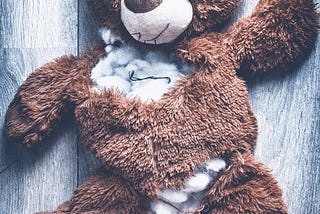 A teddy bear that has been torn apart and has stuffing exposed from large rips and tears.