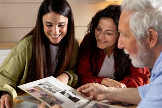 An elderly man and two young women looking at a photo album.