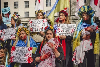 Women wearing flower crowns hold Ukrainian flags and handmade signs protesting the war.