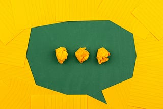 Three crumpled yellow papers on green surface surrounded by yellow lined papers