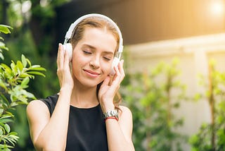 A girl wearing black sleeveless headphones enjoying music with closed eyes