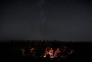 People sitting around a starry night camp fire
