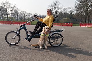 An old woman on an accessible tricycle with a guide dog beside her