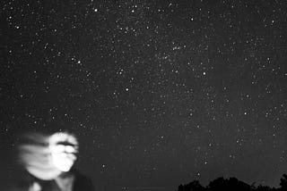 A ghostly male figure at night with a sky full of stars behind them