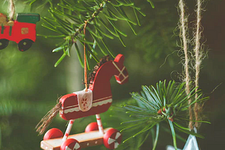 A red wooden horse decoration hangs on a Christmas tree.