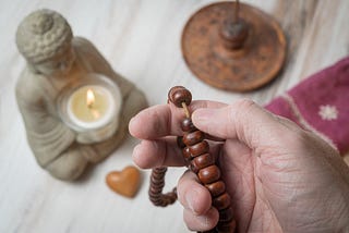 An overhead view of small Buddhist meditation shrine: pottery buddha with candle, incense holder, and a hand holding a Buddhist Mala (prayer beads)