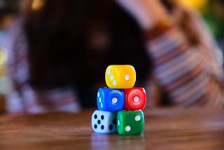 A stack of dice or a board game sitting on a table with a person behind them.