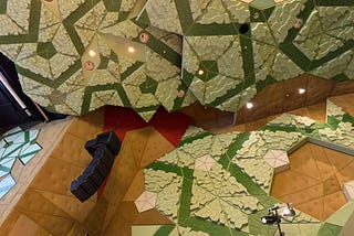 A tesselation of green triangles and wooden walls with ceiling mounted lights.