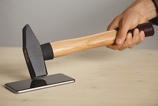 A photo of a man hitting a smartphone with a hammer.