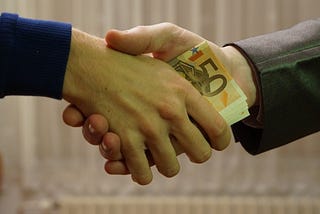 Image of money being exchanged via a handshake