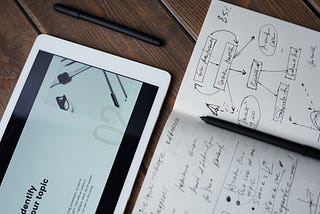 Photo of an ipad and a pen on top of a notebook.