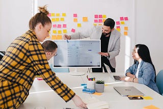 People in a brainstorming meeting with notes on the wall behind them.