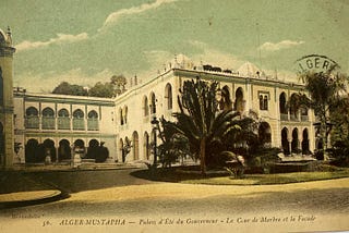 Colorized postcard showing the governor’s palace in Algiers in 1912. The palace is a two-story white building in the moorish style of artchitecture.