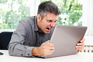 A man hunched over his laptop, screaming at it.